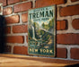 A vintage-style metal sign for Robert H. Treman State Park in New York, featuring a scenic landscape with a waterfall and a bridge.
