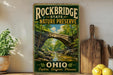 A vintage-style sign for Rockbridge State Nature Preserve, featuring a scenic image of a stone bridge surrounded by lush greenery.