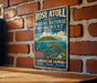 A vintage-style metal sign for Rose Atoll Marine National Monument, featuring an illustration of a tropical island and marine life, mounted on a brick wall.