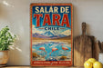 A vintage-style metal sign with a colorful illustration of a lake, mountains, and flamingos, advertising Salar de Tara, Chile.