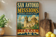 A vintage-style sign for San Antonio Missions National Historical Park, featuring an illustration of the Mission bells and the Mission bell tower, with the text "SAN ANTONIO MISSIONS NATIONAL HISTORICAL PARK" and "TEXAS" below.