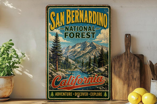 A vintage-style sign for the San Bernardino National Forest in California, featuring a scenic mountain landscape and the text "San Bernardino National Forest California Adventure - Discover - Explore".