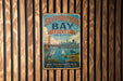 A vintage-style metal sign for San Francisco Bay, featuring a cityscape and a crane, is displayed on a wooden wall.