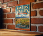 A vintage-style metal sign for San Luis Valley, Colorado, featuring a scenic landscape with mountains, a river, and a small town.