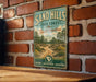 A vintage-style metal sign for the Sand Hills State Forest in South Carolina, featuring a scenic illustration of a dirt road surrounded by trees and vegetation.