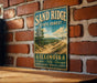 A vintage-style metal sign for the Sand Ridge State Forest in Illinois, featuring a scenic landscape with pine trees and a dirt path.