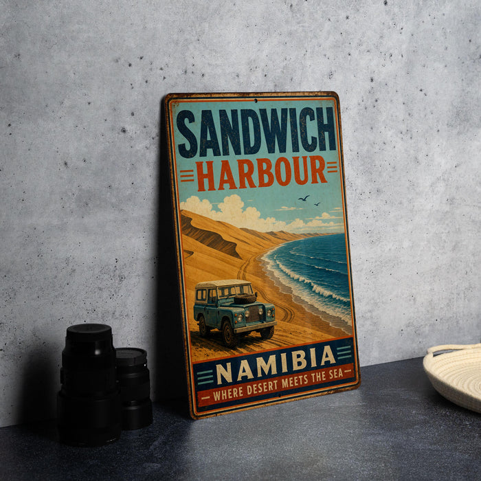 A vintage-style metal sign advertising Namibia, featuring a desert landscape with a car and the text "Sandwich Harbour Namibia - Where desert meets the sea".