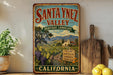 A vintage-style metal sign for Santa Ynez Valley, California, featuring a scenic landscape with vineyards, mountains, and a church.