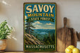 A vintage-style sign for Savoy Mountain State Forest in Massachusetts, featuring a scenic mountain landscape with pine trees and a lake.