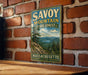 A vintage metal sign for Savoy Mountain State Forest in Massachusetts, featuring a scenic mountain landscape with pine trees and a lake.