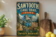 A vintage-style metal sign for the Sawtooth Lake Trail in Idaho, featuring a scenic mountain landscape with a trail sign and the text "Explore The Sawtooth Mountains".