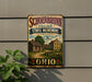 a vintage-style metal sign with a historical village scene, mounted on a wall.