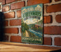 A vintage-style sign for the Schuykill River Greenways National Heritage Area in Pennsylvania, featuring a scenic illustration of a river and lush greenery.