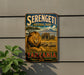 A vintage-style metal sign for Serengeti National Park in Tanzania, featuring an illustration of a lion and elephants in a savanna landscape.