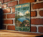 A vintage-style metal sign for Shawme-Crowell State Forest in Massachusetts, featuring a scenic landscape with a lake, pine trees, and a rocky outcrop.