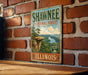 A vintage-style metal sign for Shawnee National Forest in Illinois, featuring a scenic landscape with a river and a cliff.