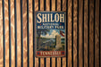 A vintage metal sign for Shiloh National Military Park in Tennessee, featuring a cannon and a monument, is displayed on a wooden wall.