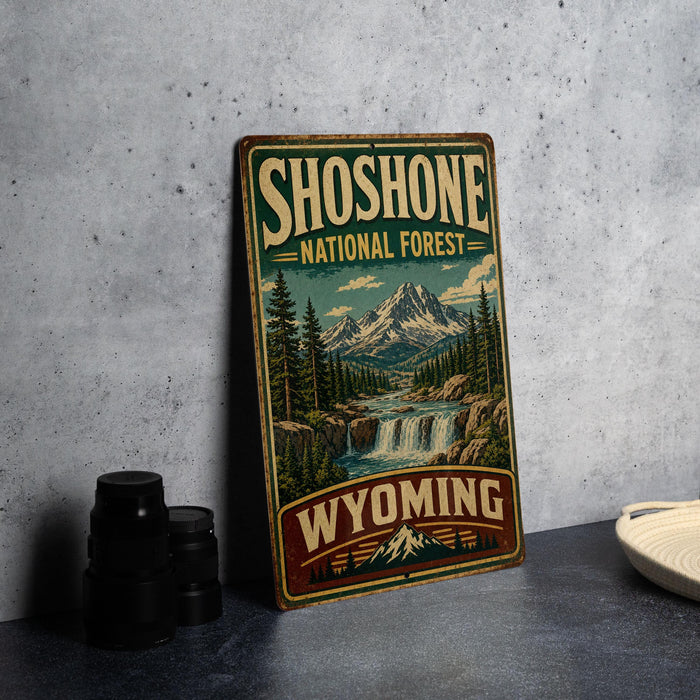 A vintage-style sign for Shoshone National Forest in Wyoming, featuring a scenic mountain landscape with a waterfall.