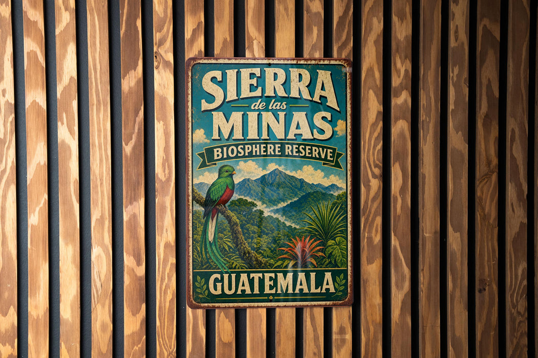 A vintage-style metal sign with the text "SIERRA de las MINAS BIOSPHERE RESERVE GUATEMALA" and an illustration of a colorful bird perched on a tree.