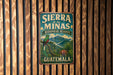 A vintage-style metal sign with the text "SIERRA de las MINAS BIOSPHERE RESERVE GUATEMALA" and an illustration of a colorful bird perched on a tree.