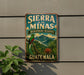 A vintage-style metal sign with the text "SIERRA de las MINAS BIOSPHERE RESERVE GUATEMALA" and an illustration of a colorful bird perched on a tree branch, set against a backdrop of lush tropical vegetation.