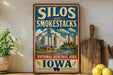 A vintage-style sign for Silos and Smokestacks, located in the National Heritage Area of Iowa, with a farm scene and industrial buildings in the background.