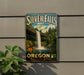 A vintage-style metal sign for Silver Falls State Park in Oregon, featuring a waterfall surrounded by lush greenery and flowers.
