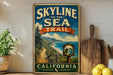A vintage-style metal sign that reads "SKYLINE TO THE SEA TRAIL" and "CALIFORNIA", with a scenic illustration of a coastal path leading to a beach.