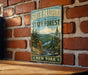 A vintage-style metal sign for South Bradford State Forest in New York, featuring a scenic landscape with pine trees, mountains, and a river.
