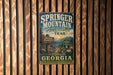 A vintage trail sign for the Springer Mountain Approach Trail in Georgia, featuring a scenic mountain landscape and inviting visitors to explore the region.