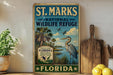 A vintage-style sign for St. Marks National Wildlife Refuge in Florida, featuring a bird and palm trees, is displayed on a shelf next to a wooden cutting board and some lemons.