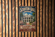 A vintage metal sign for Stanton Hall in Mississippi, featuring a large building with columns and a blue sky background.