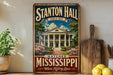 A vintage-style metal sign for Stanton Hall in Natchez, Mississippi, featuring a large illustration of the historic building surrounded by trees and flowers.