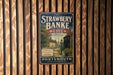 A vintage metal sign for the Strawberry Banke Museum, featuring a scenic image of a historic neighborhood in the past lane.