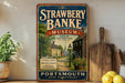A vintage-style sign for the Strawberry Banke Museum in Portsmouth, New Hampshire, featuring a scenic illustration of a historic neighborhood.