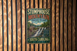 A vintage metal sign for Stumphouse Mountain Heritage Preserve in South Carolina, featuring a scenic illustration of a waterfall and a wooden cabin.