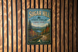 A vintage-style metal sign for Sugar Hill State Forest in New York, featuring a scenic landscape with pine trees and a winding road.
