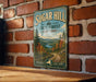 A vintage-style metal sign for Sugar Hill State Forest in New York, featuring a scenic landscape with a winding road and pine trees.