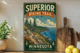 A vintage-style sign for the Superior Hiking Trail in Minnesota, featuring a scenic mountain landscape with pine trees and a winding trail.