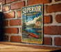 A vintage-style metal sign for Superior National Forest in Minnesota, featuring a canoe on a lake surrounded by mountains and pine trees.