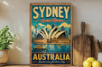 A vintage-style metal sign displaying the Sydney Opera House and Australia, with a wooden paddle and lemons in the foreground.