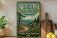 A vintage-style metal sign for the Taconic Trail State Forest in Massachusetts, featuring a scenic mountain landscape with a winding path and wildflowers.