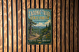 A vintage-style metal sign for the Taconic Trail State Forest in Massachusetts, featuring a scenic landscape with a path, trees, and mountains.