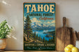 A vintage-style sign for the Tahoe National Forest in California, featuring a scenic mountain landscape with pine trees, a lake, and a wooden paddleboard.