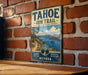 A vintage-style metal sign for the Tahoe Rim Trail in Nevada, featuring a scenic mountain landscape and a trail leading to a lake.
