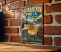 A vintage-style metal sign for Tahquamenon Falls State Park in Michigan, featuring a waterfall and forest scenery.