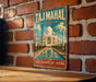 A vintage-style metal sign displaying the Taj Mahal, a famous landmark in India, mounted on a brick wall.