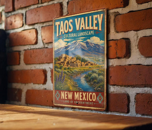 A vintage-style sign for the Taos Valley in New Mexico, featuring a scenic landscape with mountains, buildings, and a river.
