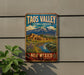 A vintage-style metal sign advertising the Taos Valley Cultural Landscape in New Mexico, featuring a scenic landscape with mountains, a river, and a small village.