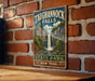 A vintage-style metal sign for Taughannock Falls, a waterfall located in New York State Park, is displayed on a brick wall.